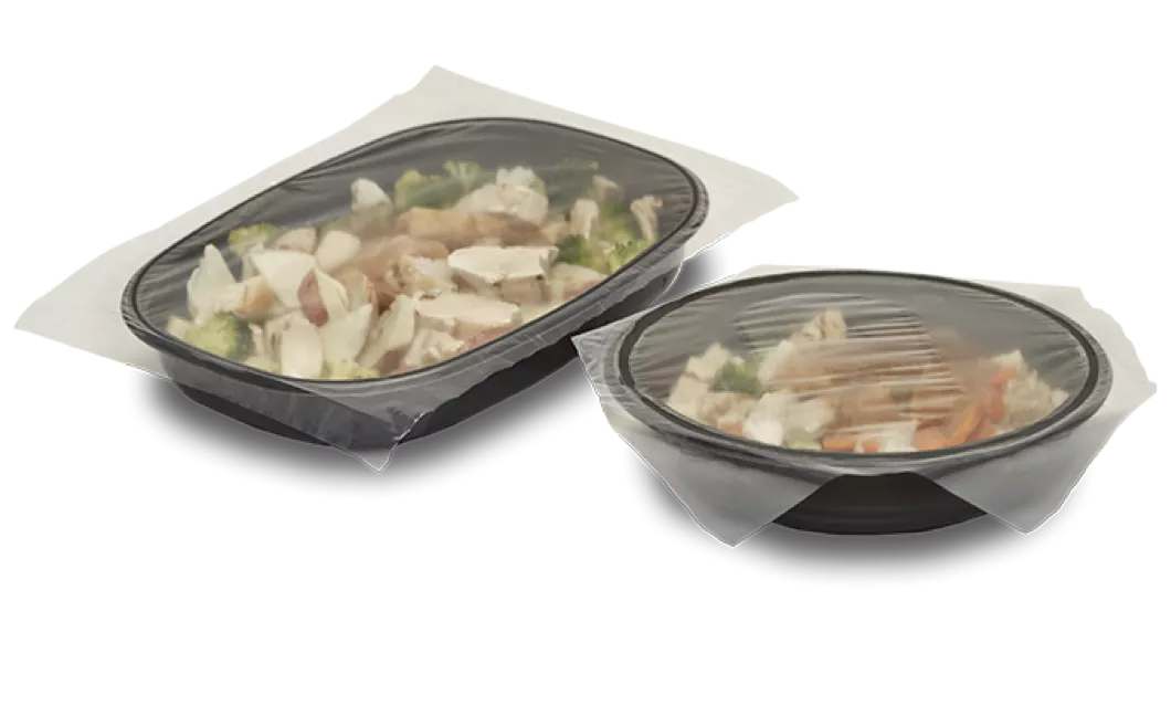 Two black CPET frozen meal trays with food and a clean lidding film over the top