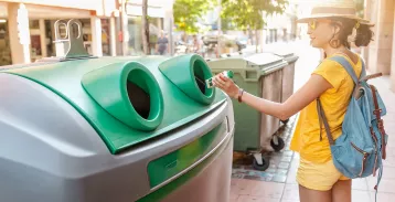 Woman throwing a plastic bottle into a recycling bin.