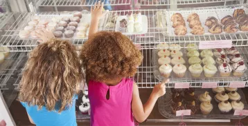 Two kids examining cupcakes in a bakery display case